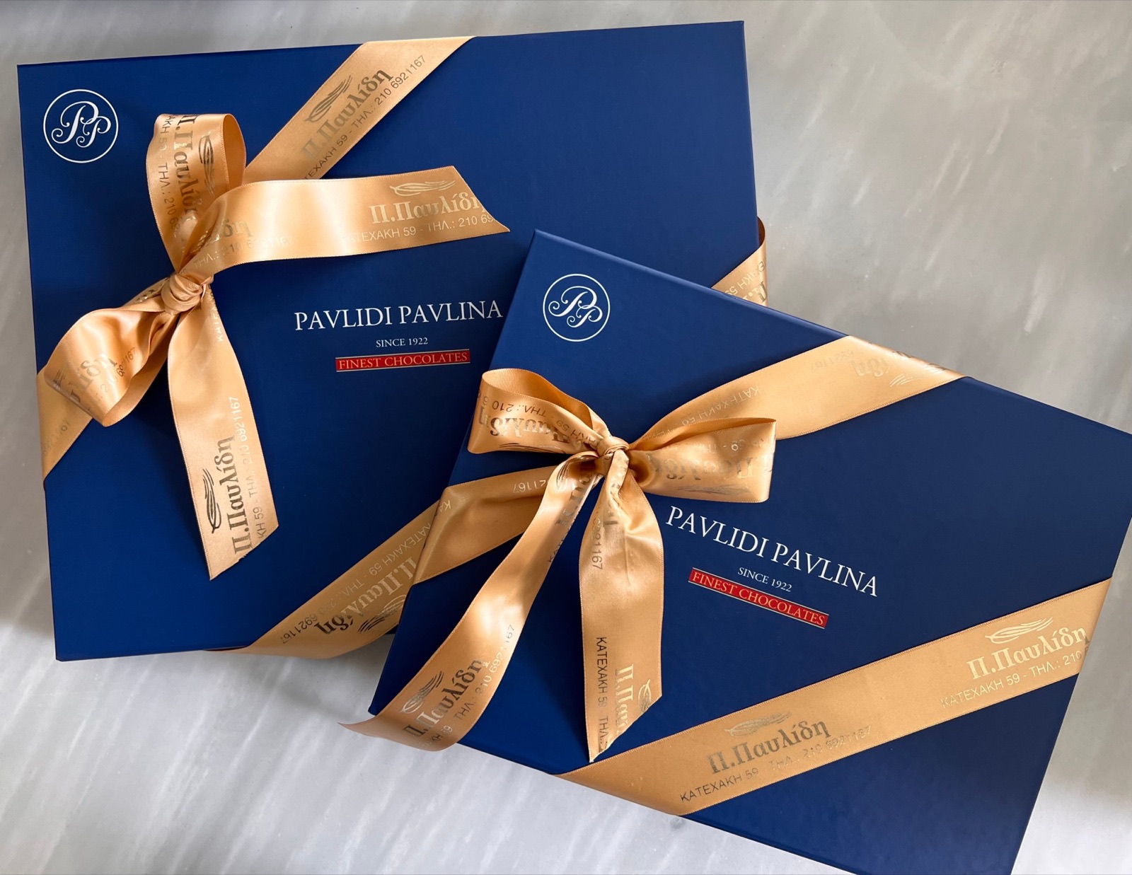 Δύο μπλε κουτιά σοκολατακίων Pavlidi Pavlina δεμένα με χρυσή κορδέλα